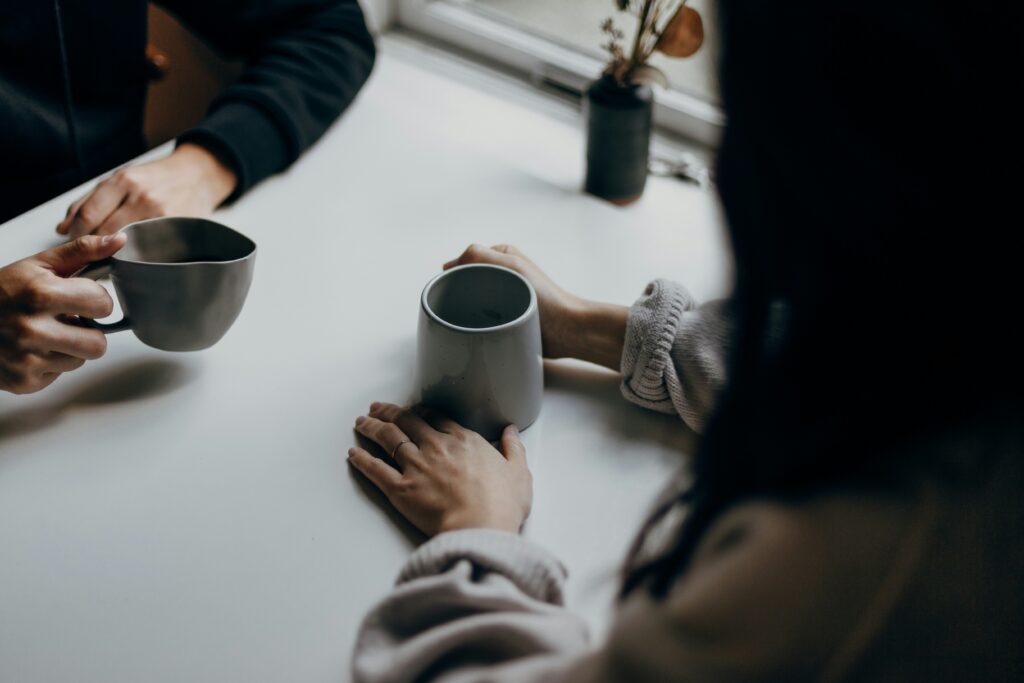 Faceless couple sitting across from each other at a table, with coffee mugs in hand, having a daily check in 